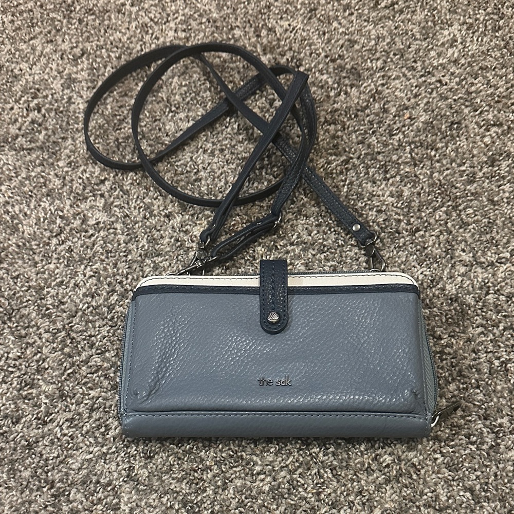The Sak Iris crossbody wallet in dusty blue leather with navy and ivory trim.